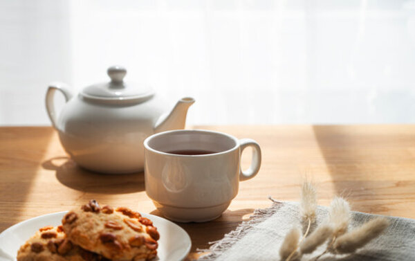 Cup of tea on a wooden table with a teapot nearby